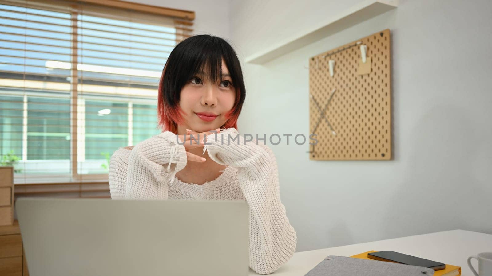 Attractive young woman using laptop computer at desk in home office. Freelancer, working remotely and technology by prathanchorruangsak