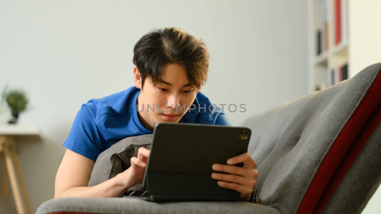 Casual asian man lying on couch hand using digital tablet. People, technology and lifestyle by prathanchorruangsak