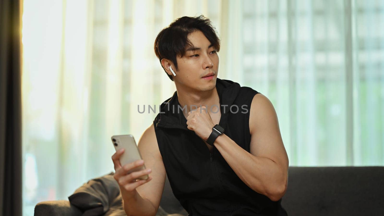 Handsome man in sportswear using smartphone, resting after working out at home. Fitness and healthy lifestyle concept.