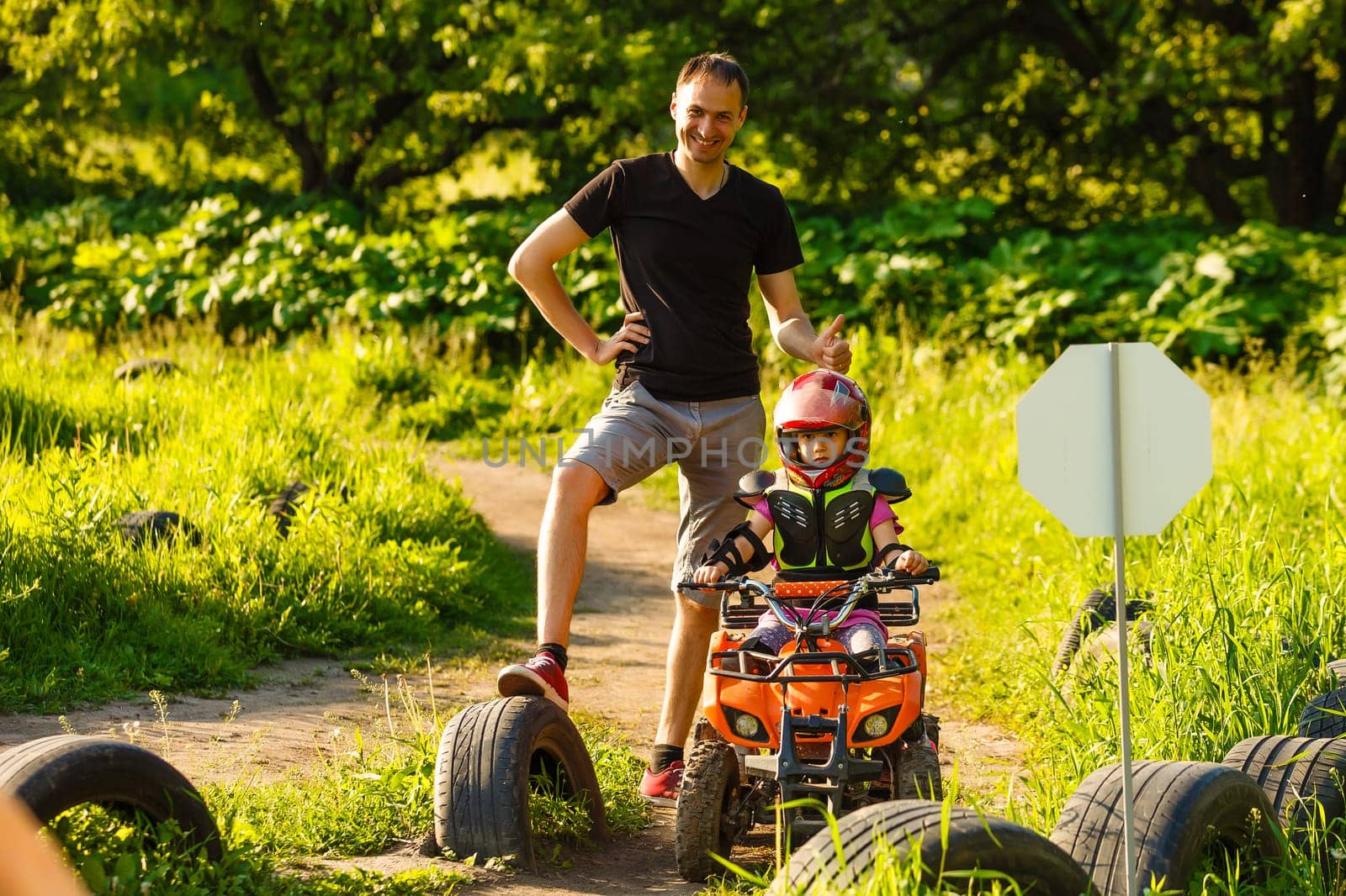 Father and daughter playing on the road at the day time. They driving on quad bike in the park. People having fun on the nature. Concept of friendly family.