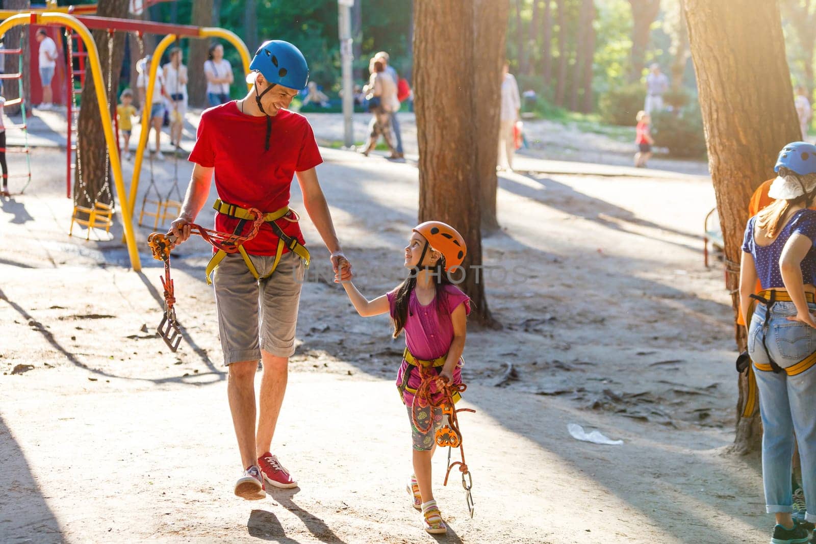 Young father helps his daughter on the obstacle in the rope park.