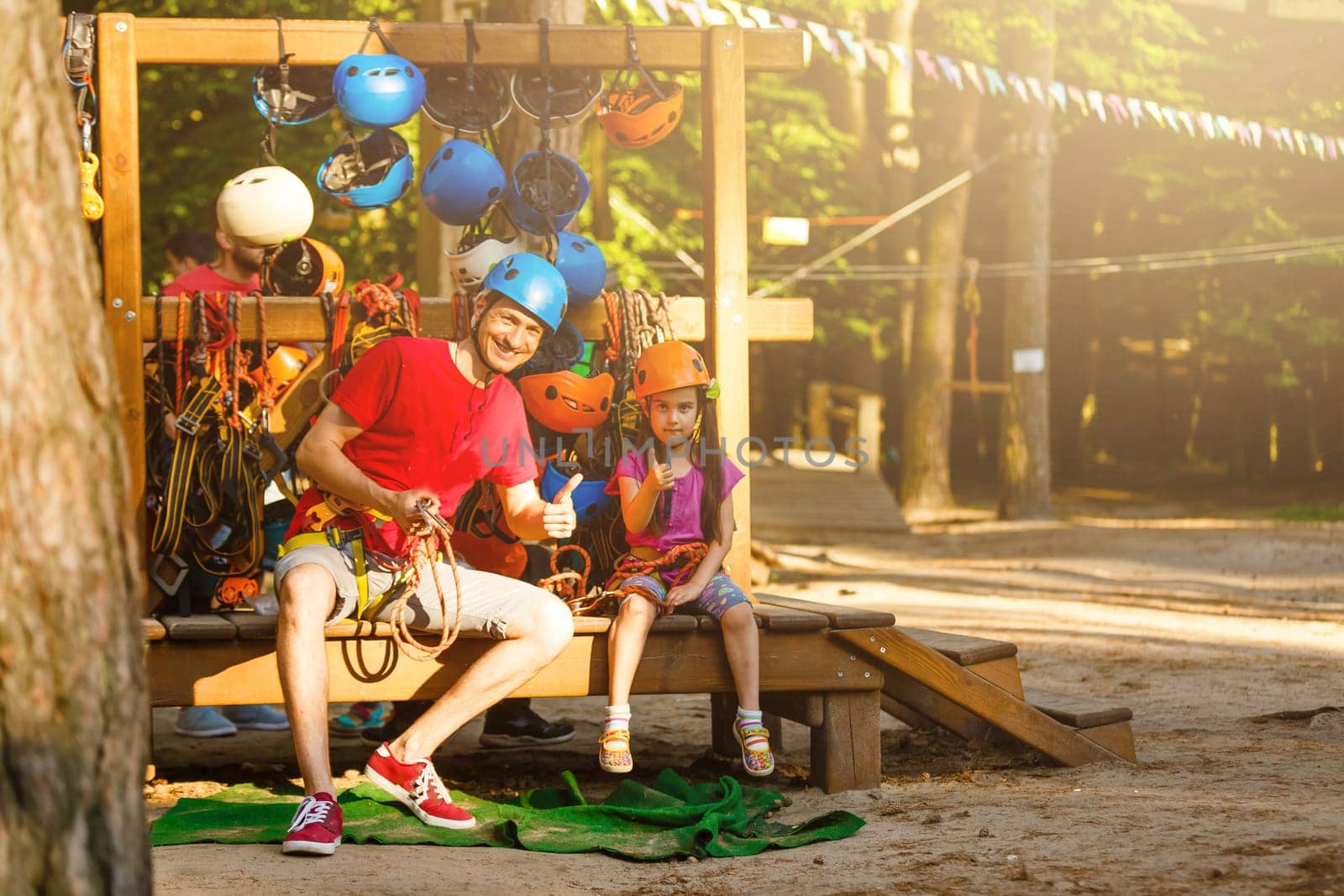 Young father helps his daughter on the obstacle in the rope park.