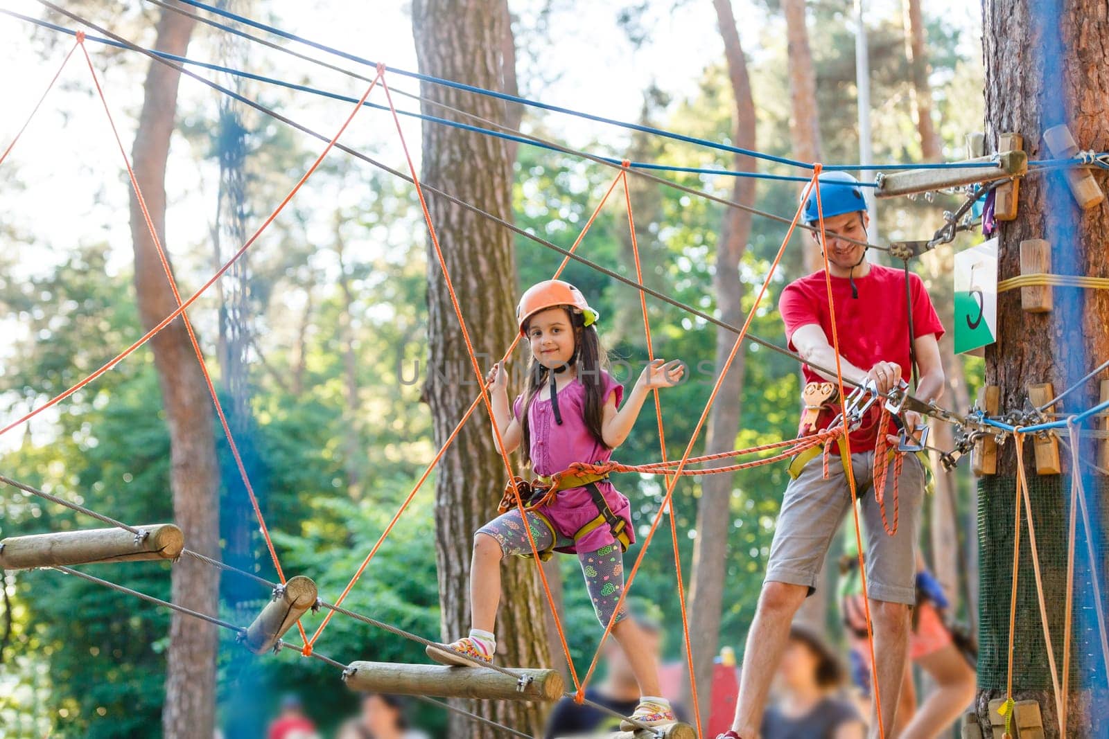 Young father helping his little daughter in the rope park