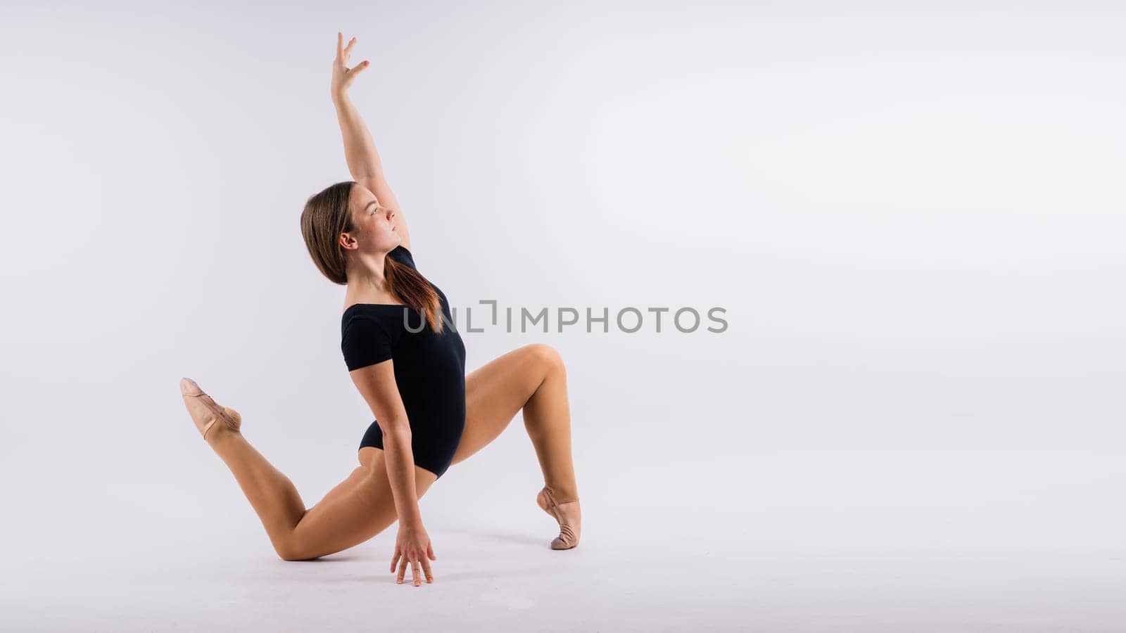 Flexible girl, rhythmic gymnastics artist jumping on white dark background. Grace in motion, action. by Zelenin
