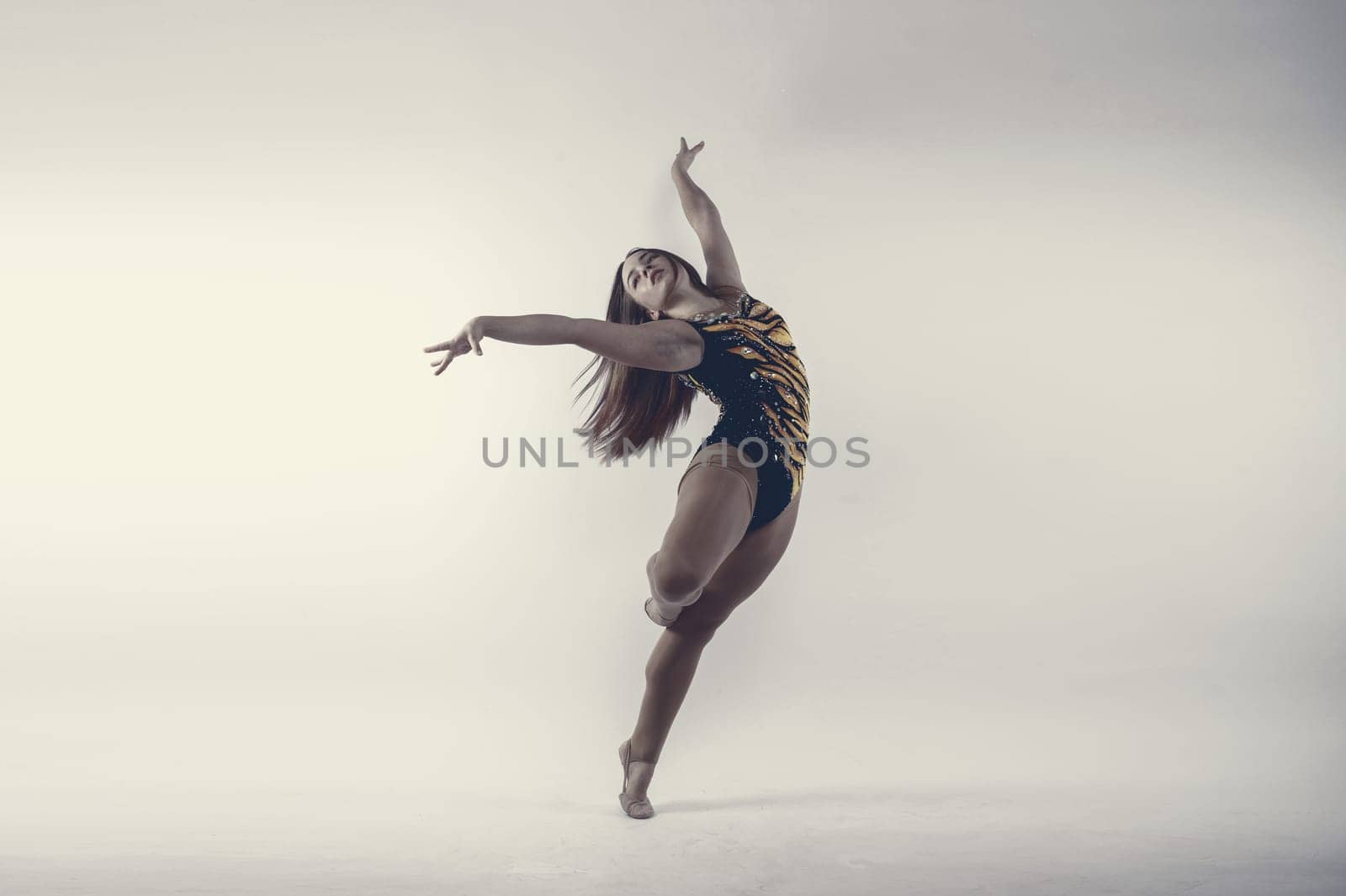 Flexible girl, rhythmic gymnastics artist jumping on white dark background. Grace in motion, action. by Zelenin