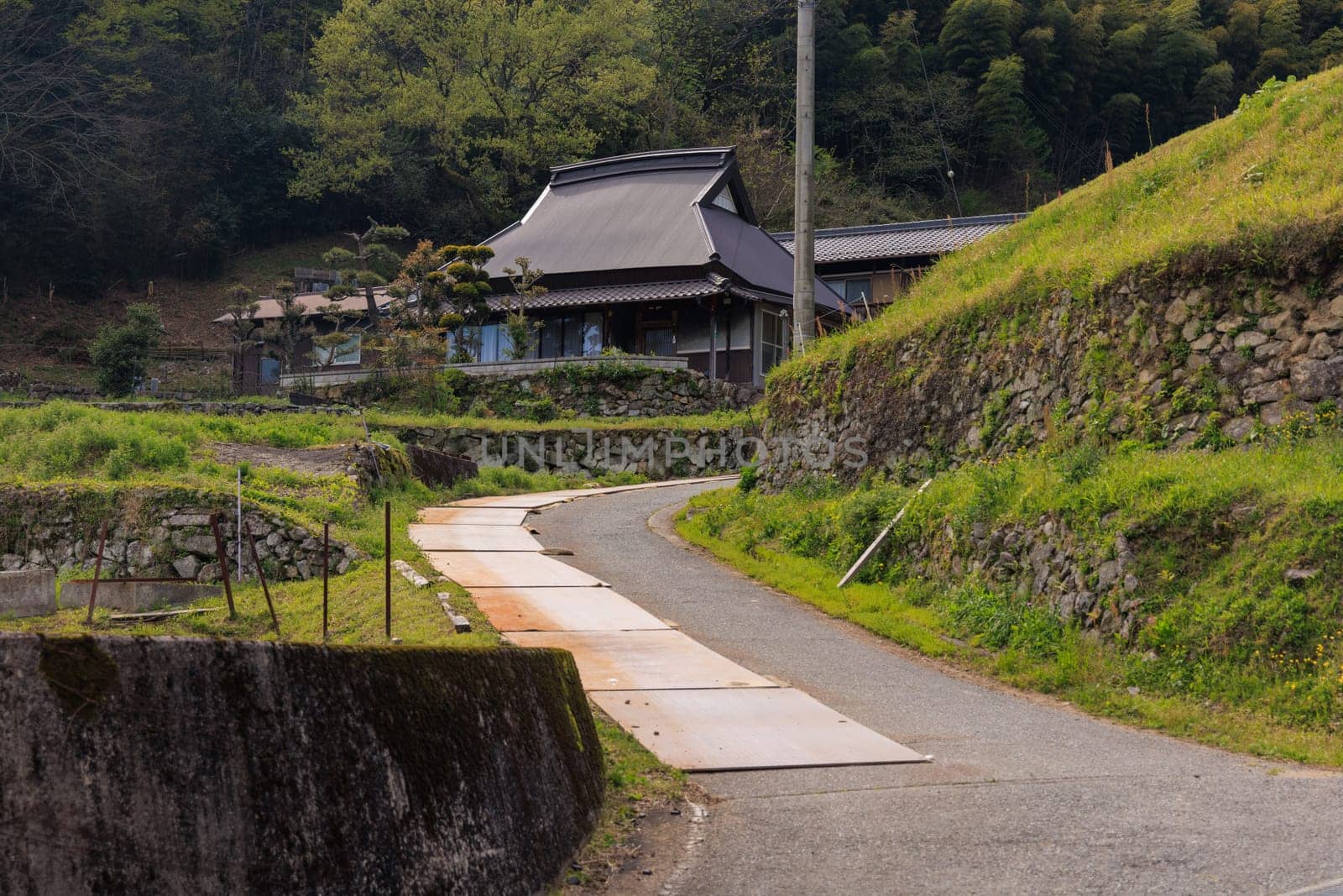 Narrow road by ancient stone wall to traditional Japanese house in rural village. High quality photo