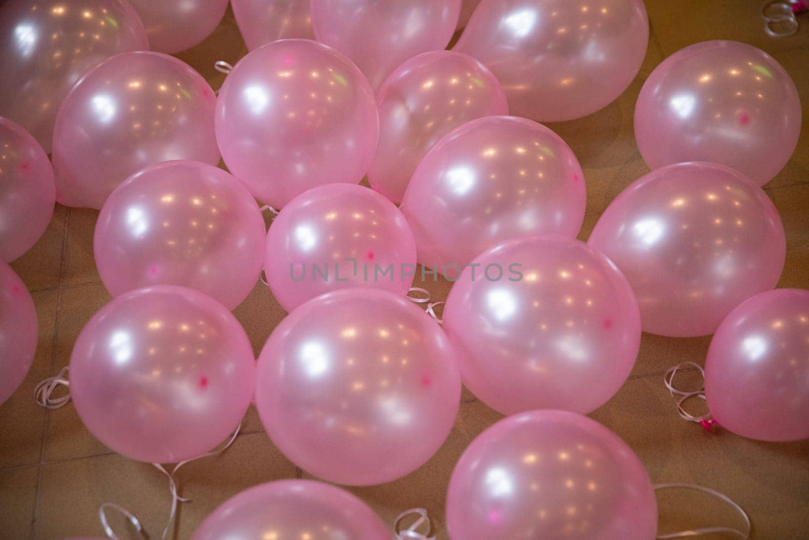 A large number of pink balloons with tied ribbons lie on the floor. An aerial view of preparations for a symposium on breast cancer prevention.