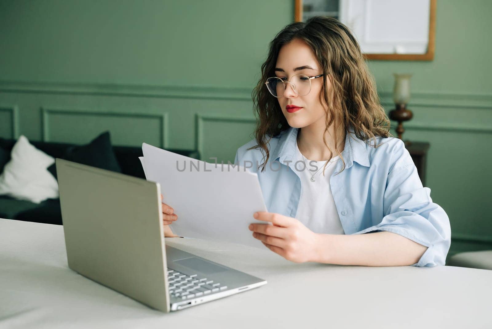 Efficient business woman managing financial data with a laptop and accounting documents in the office. Young female manager or lawyer multitasking with paperwork and laptop at work.