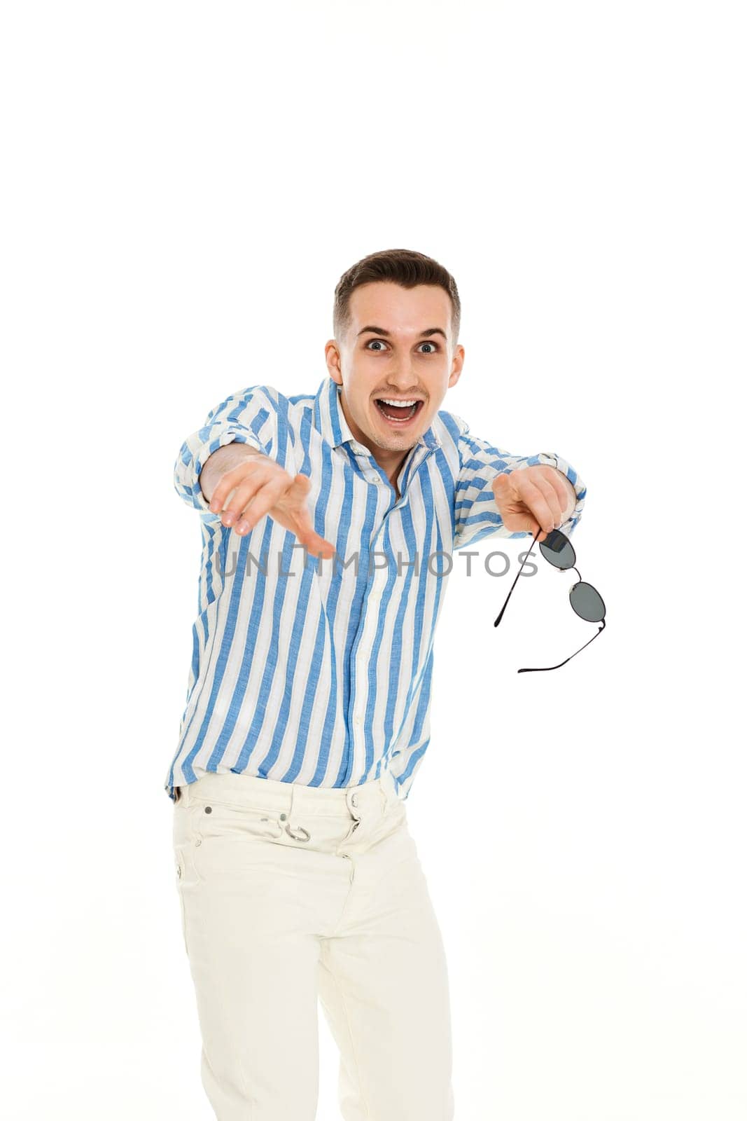 young man in sunglasses and blue striped shirt pointing finger at you isolated on white background.