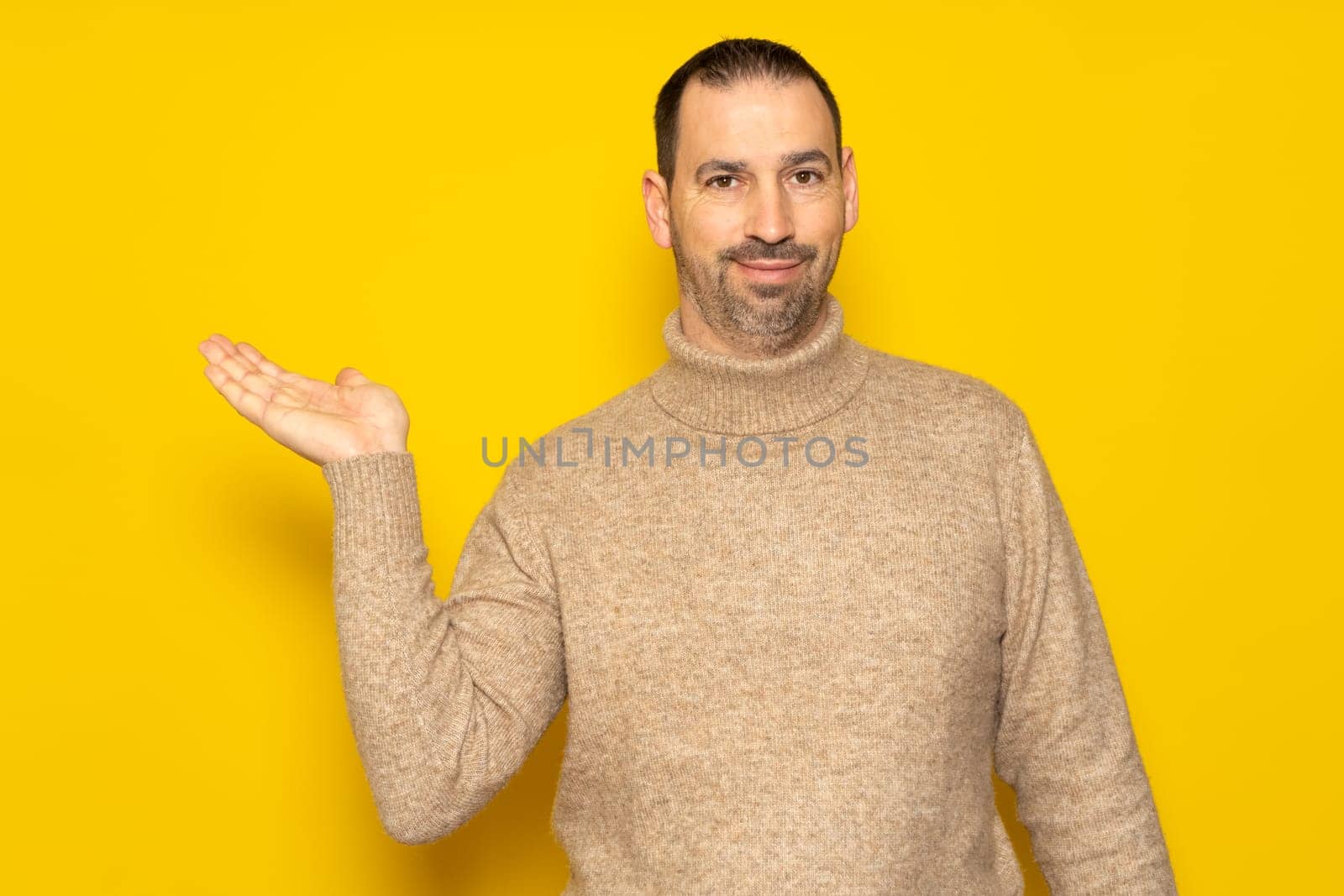 Bearded Hispanic man in his 40s wearing a beige turtleneck presenting an imaginary product in advertising concept with copy space, isolated on yellow studio background