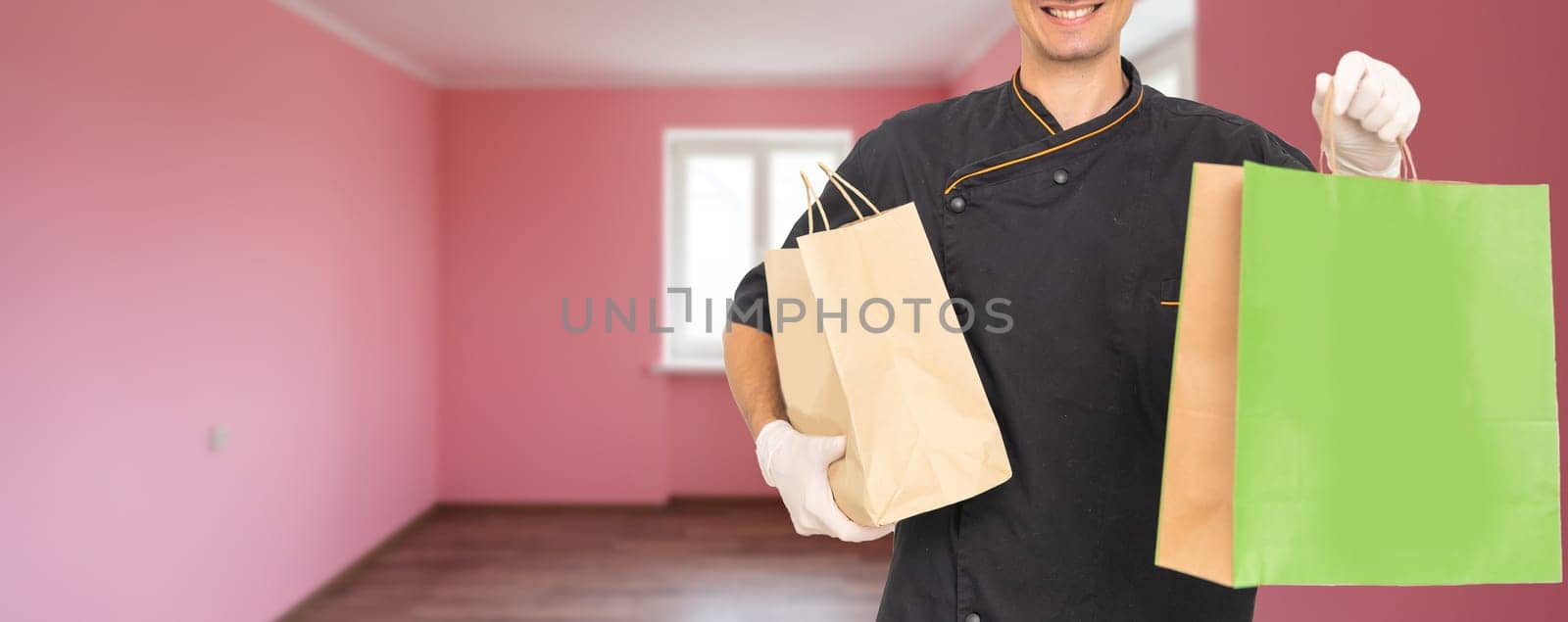 Courier holding paper bags with food, space for text. Delivery service.