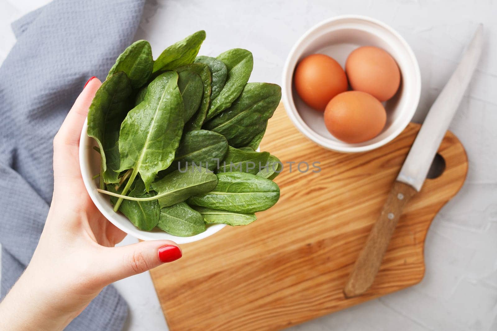 A woman's hand holds a plate with fresh organic sorrel leaves on a gray background.First spring greenery. Healthy food concept. copy space