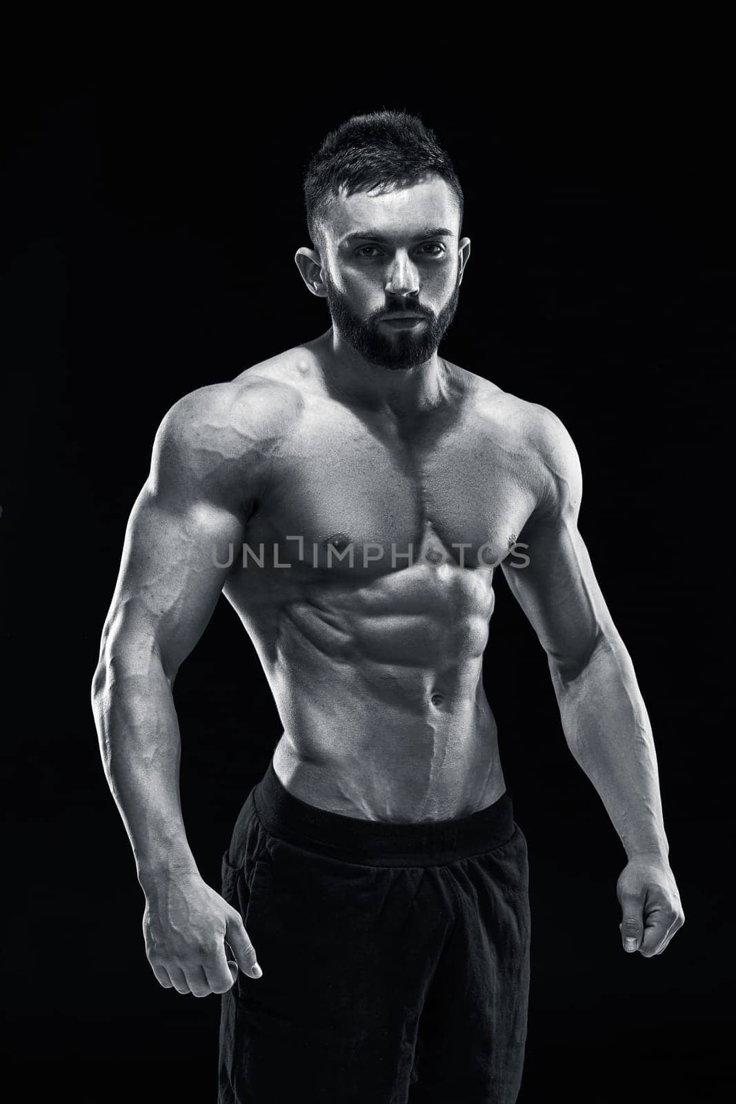 Muscular bodybuilder guy doing posing over black background. Black and white color