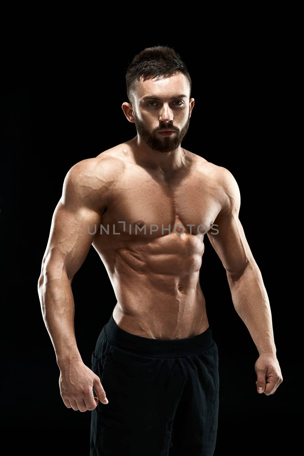 Muscular bodybuilder guy doing posing over black background.