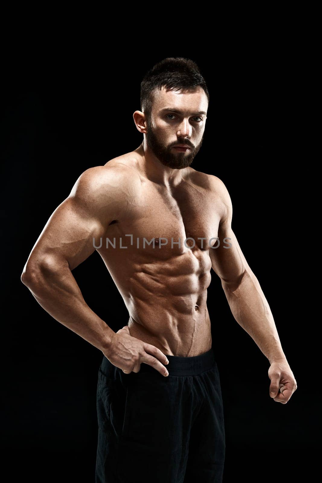 Muscular bodybuilder guy doing posing over black background.