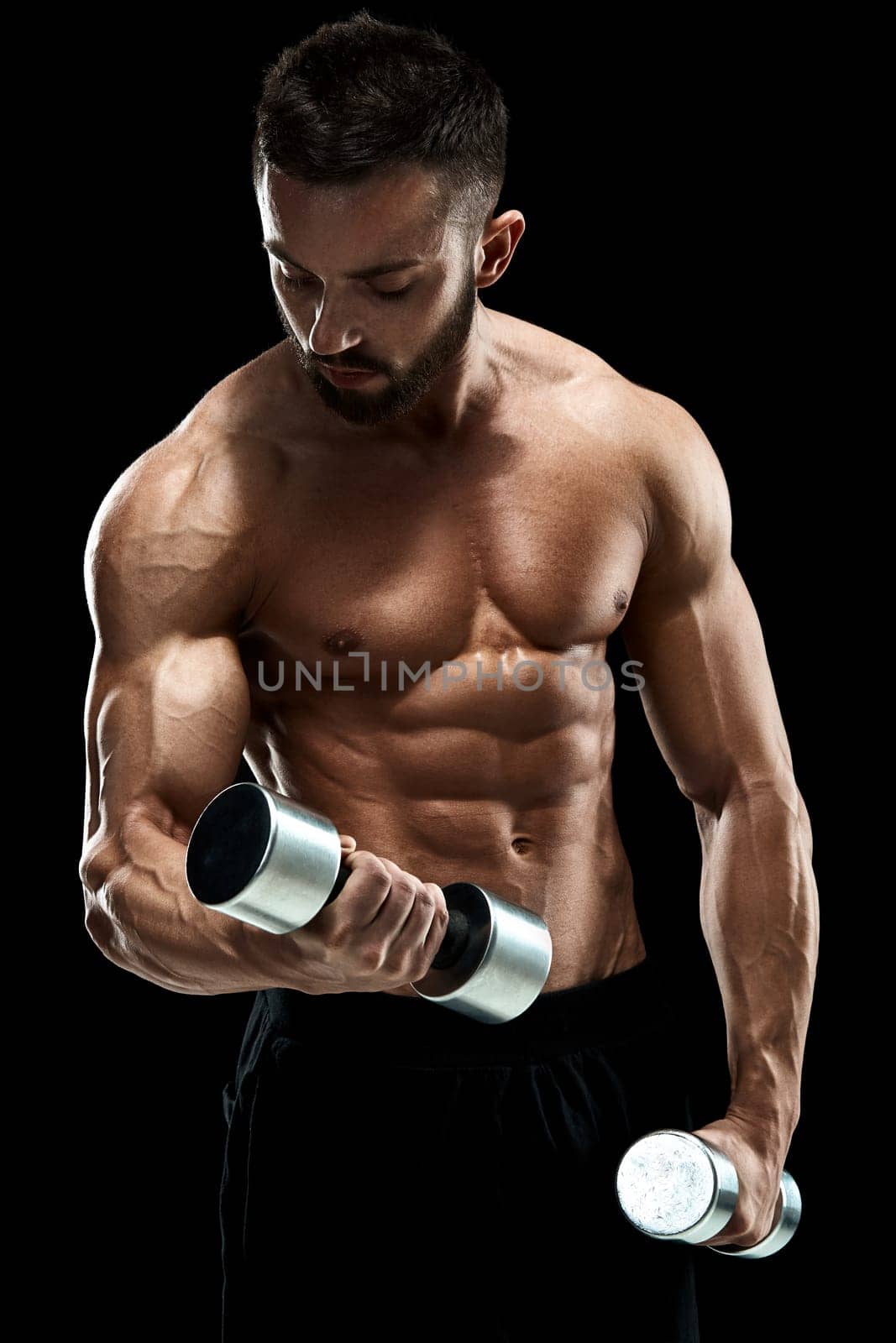 Muscular bodybuilder guy doing posing over black background. dumbbells in his hands. doing exercises