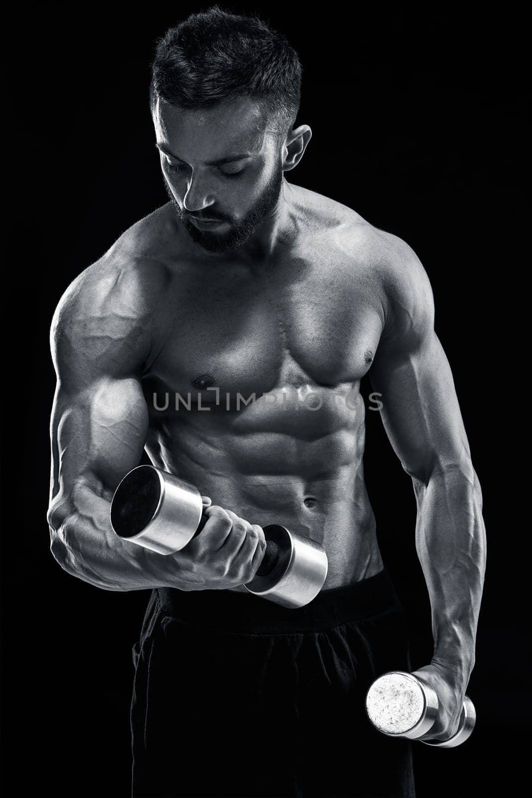 Muscular bodybuilder guy doing posing over black background. dumbbells in his hands. doing exercises. Black and white color