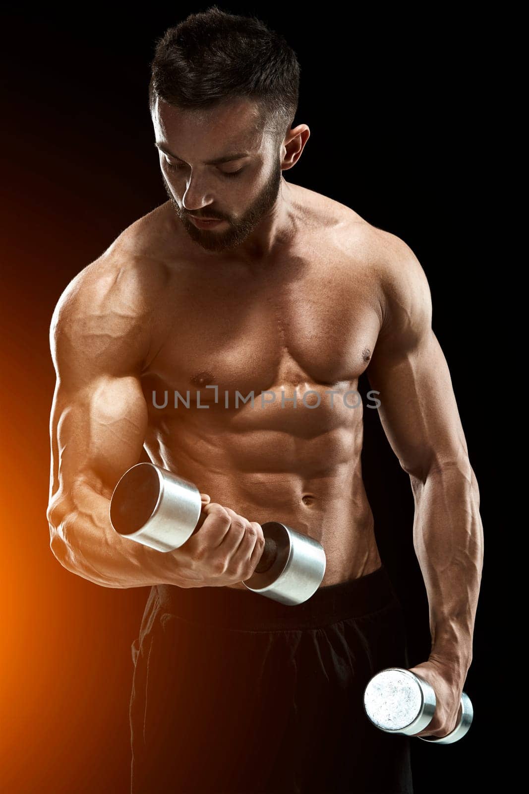 Muscular bodybuilder guy doing posing over black background. dumbbells in his hands. doing exercises. with sun flare