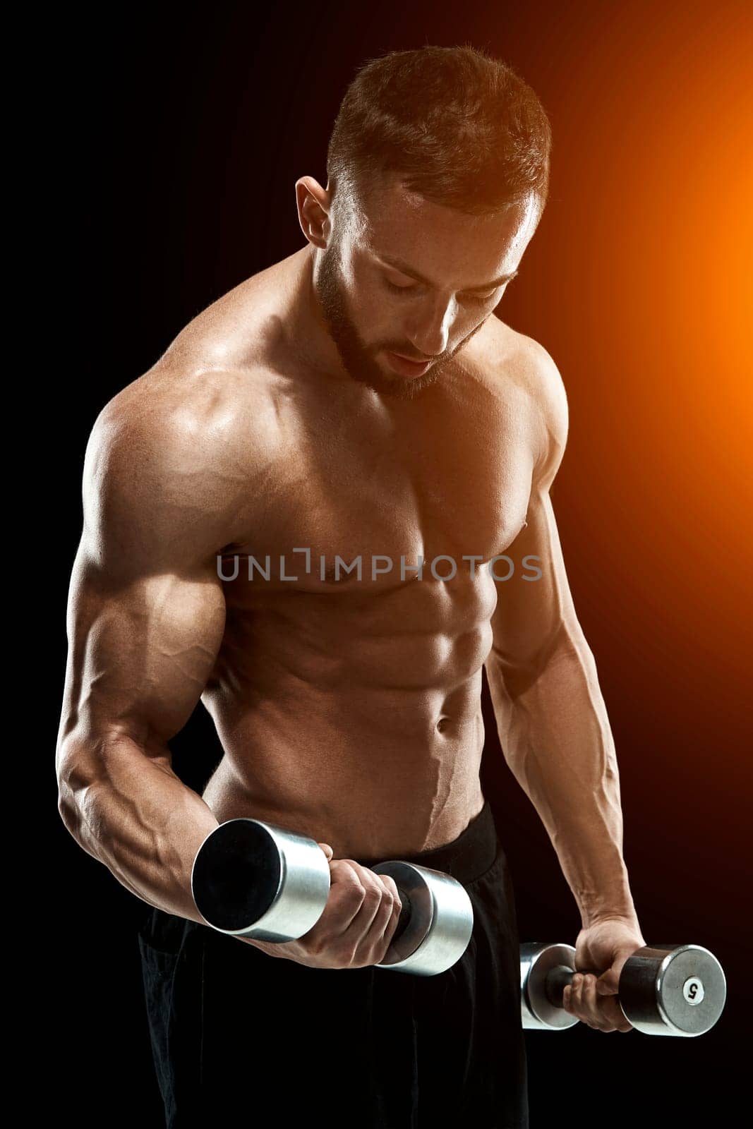 Muscular bodybuilder guy doing posing over black background. dumbbells in his hands. doing exercises. with sun flare