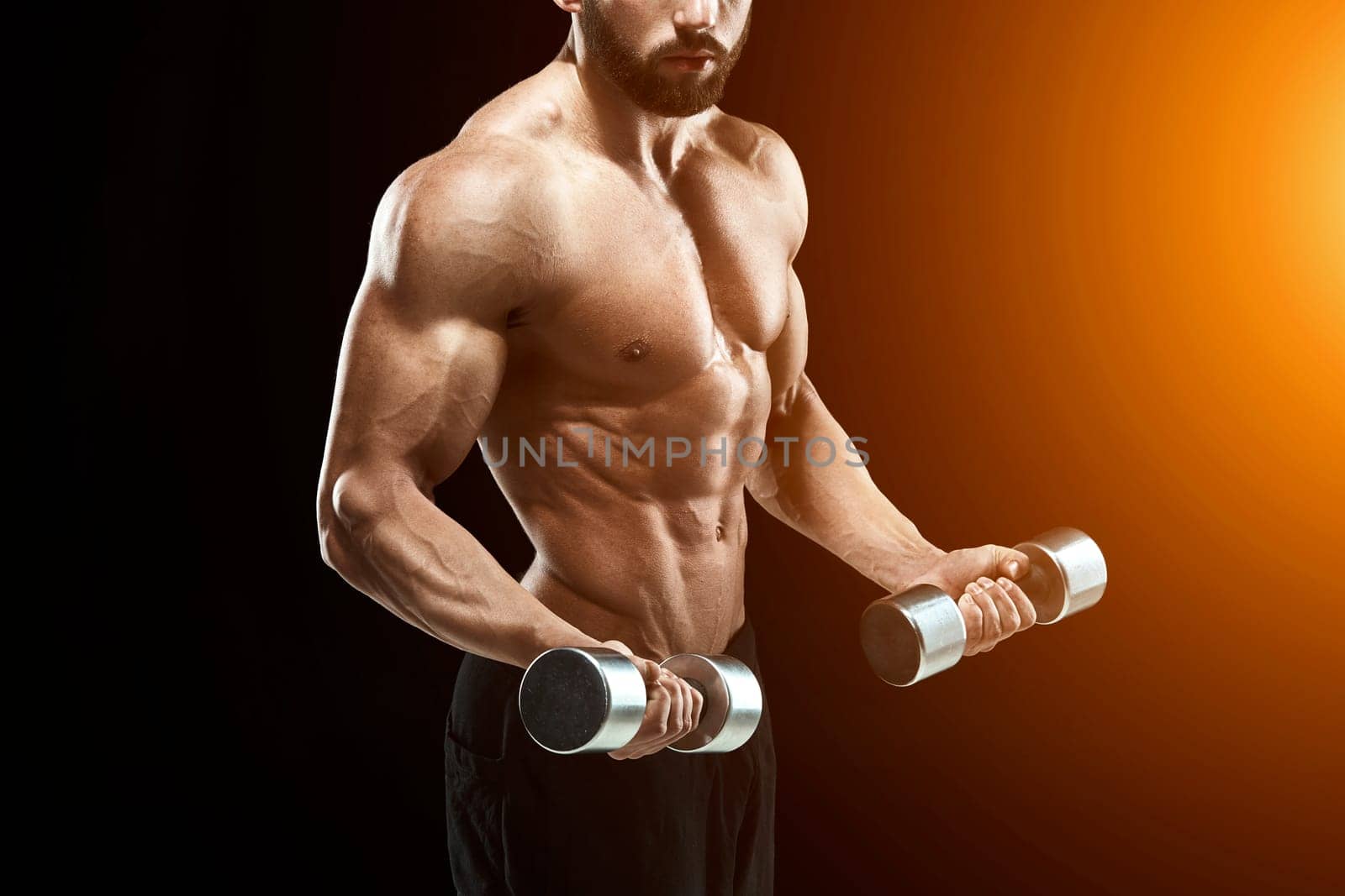 Muscular bodybuilder guy doing posing over black background. dumbbells in his hands. doing exercises. close up. with sun flare