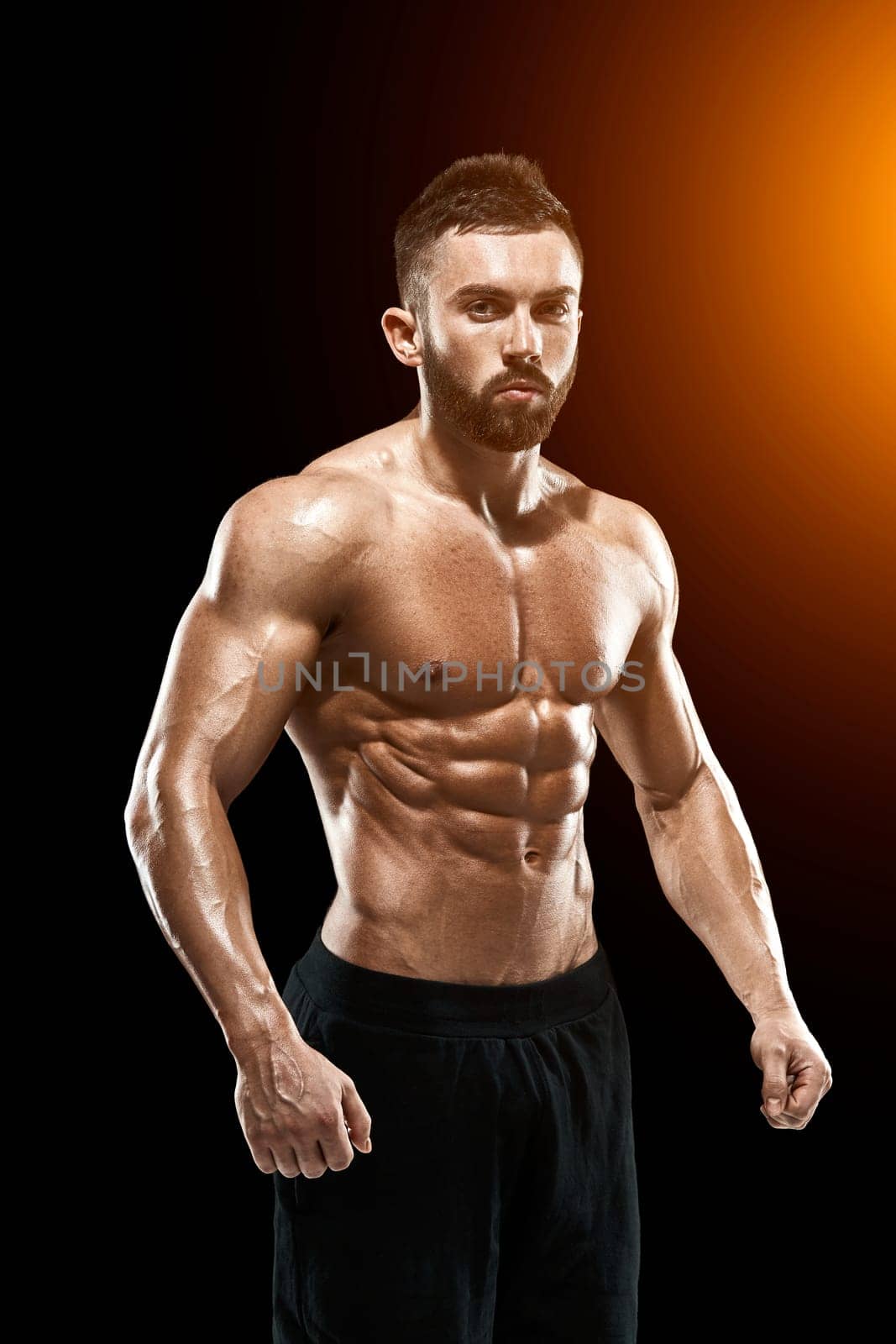 Muscular bodybuilder guy doing posing over black background.. with sun flare