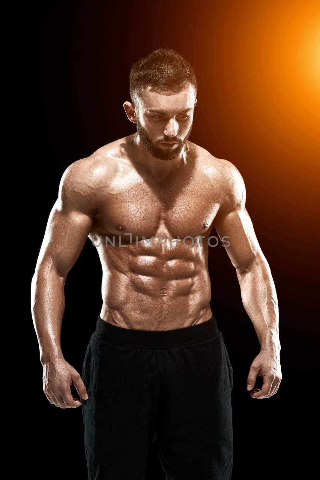 Muscular bodybuilder guy doing posing over black background.. with sun flare