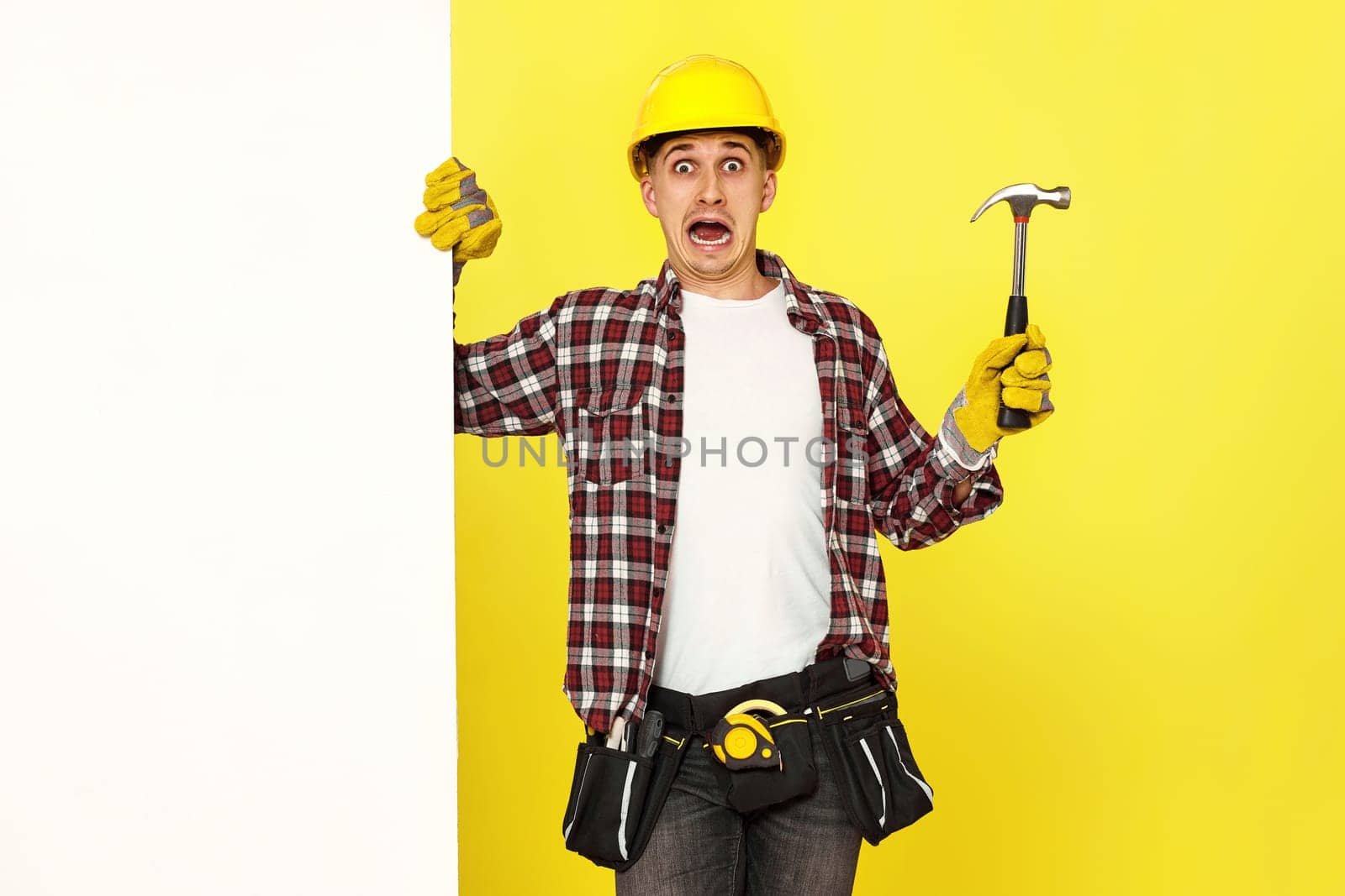 scared professional builder in work clothes in helmet holding hammer. copy space for text