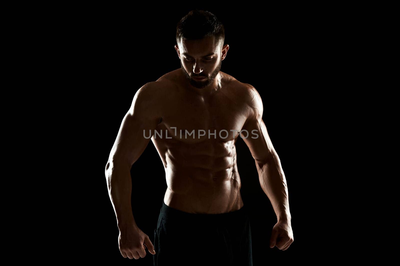 Muscular bodybuilder guy doing posing over black background.