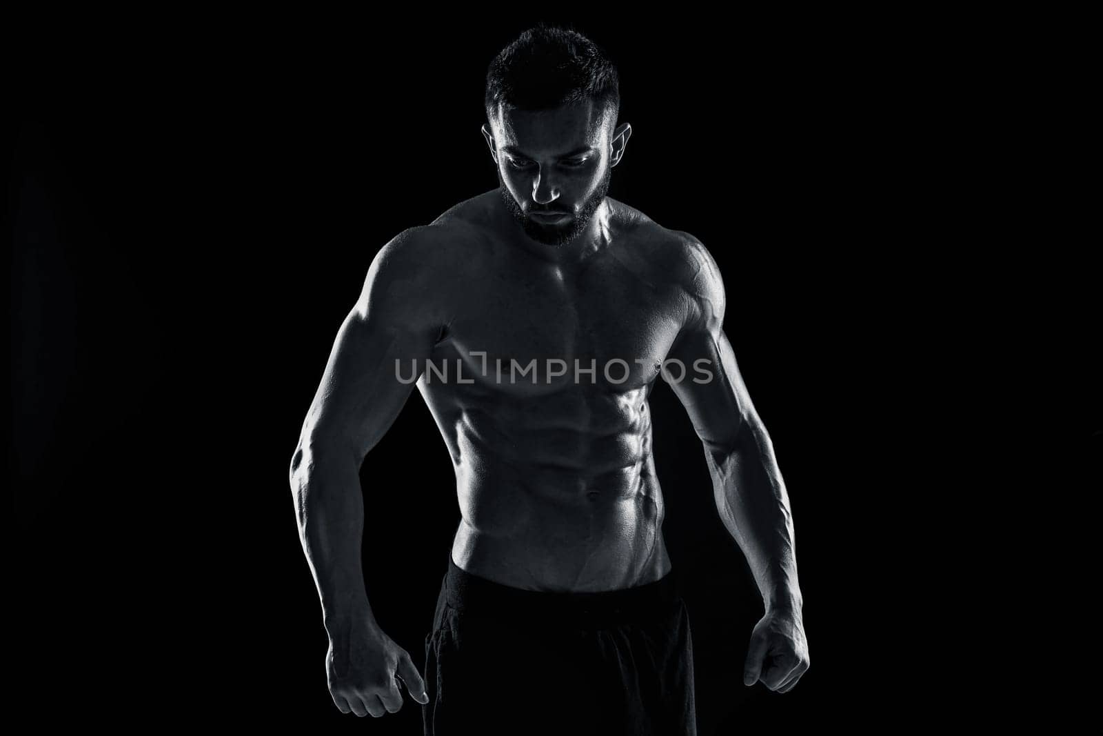 Muscular bodybuilder guy doing posing over black background. Black and white color