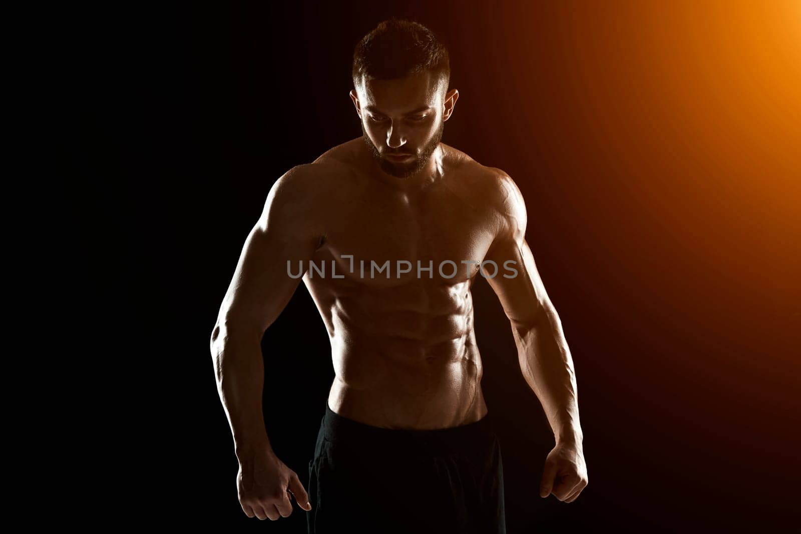 Muscular bodybuilder guy doing posing over black background.. with sun flare