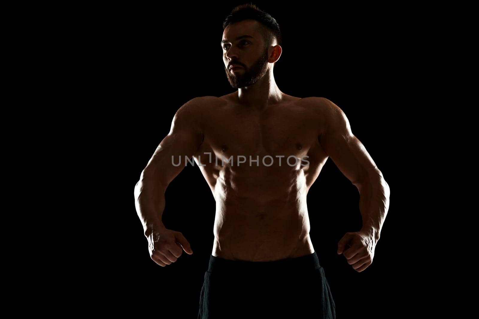 Muscular bodybuilder guy doing posing over black background.