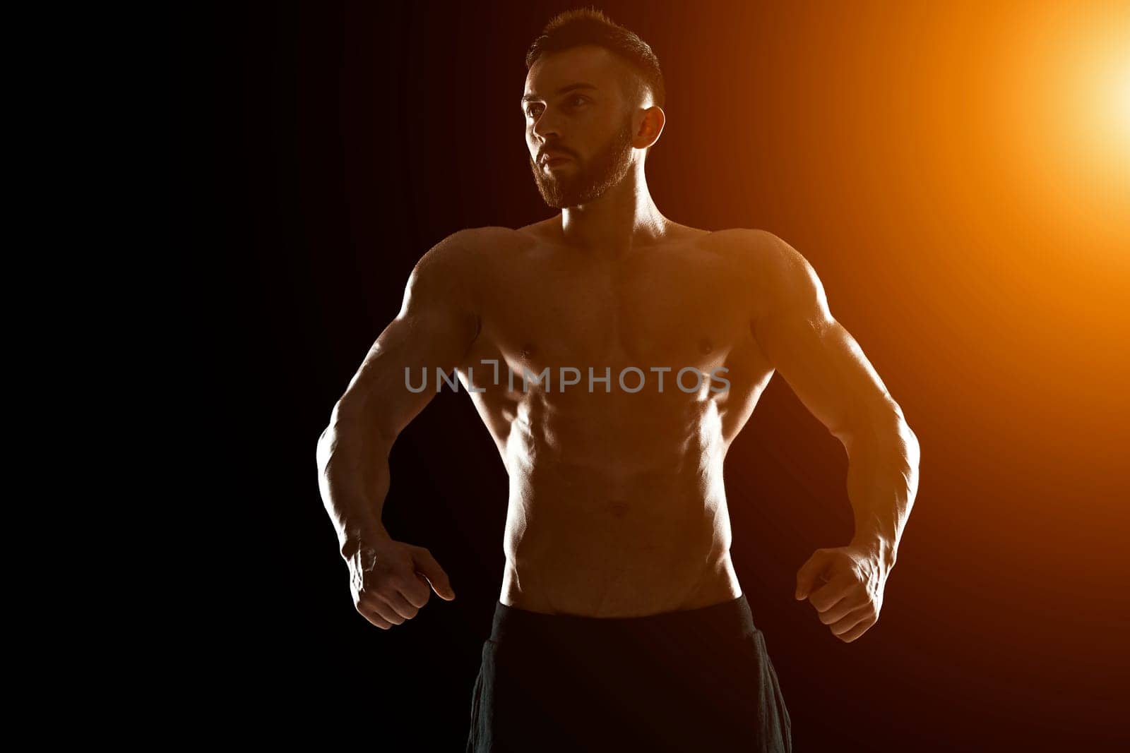 Muscular bodybuilder guy doing posing over black background.. with sun flare