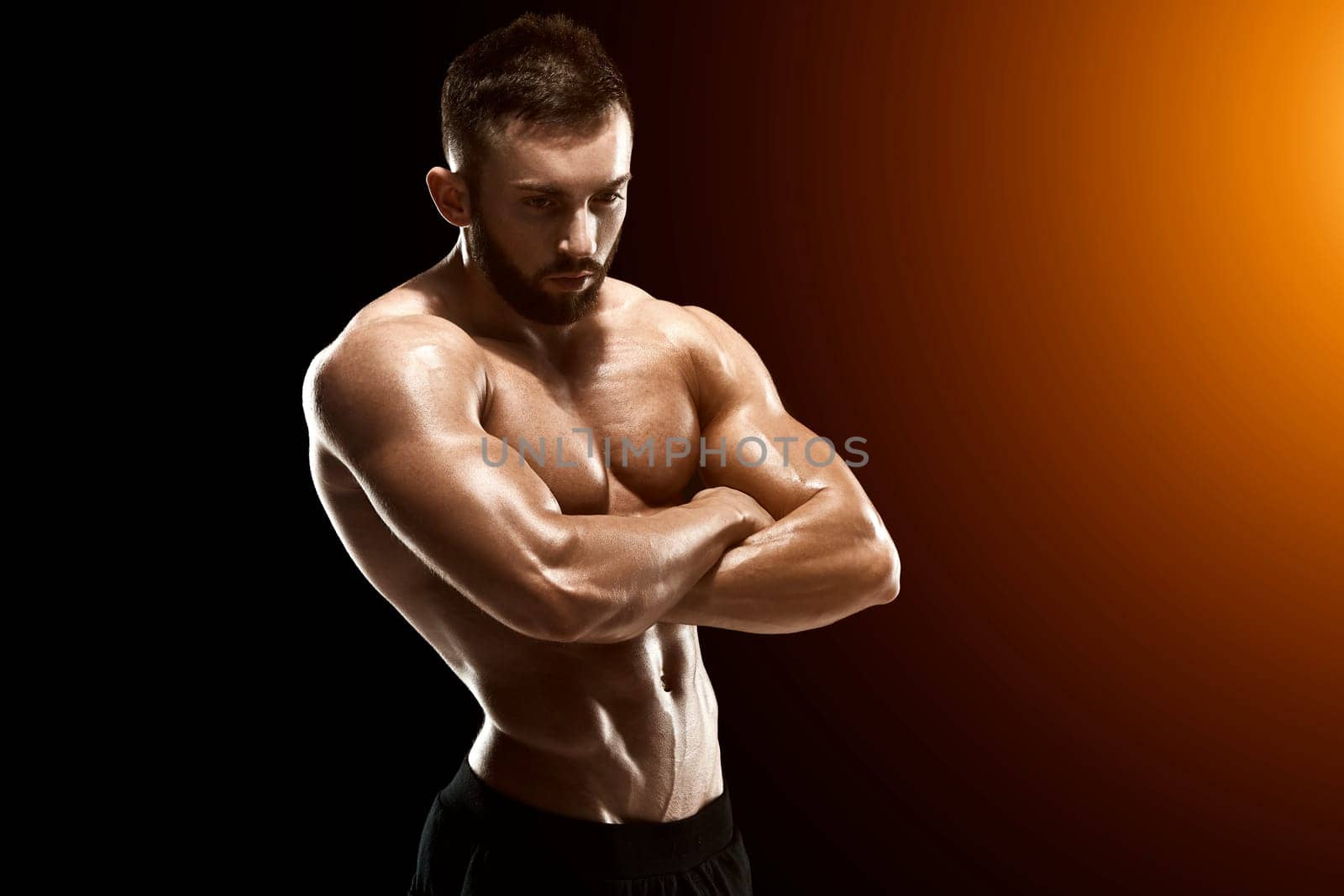 Muscular bodybuilder guy doing posing over black background.. with sun flare