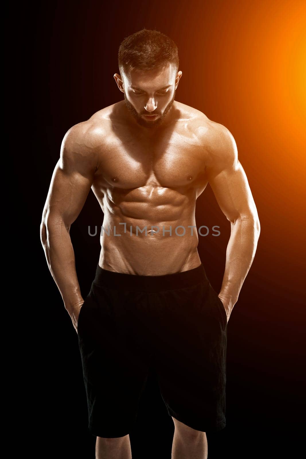 Muscular bodybuilder guy doing posing over black background.. with sun flare