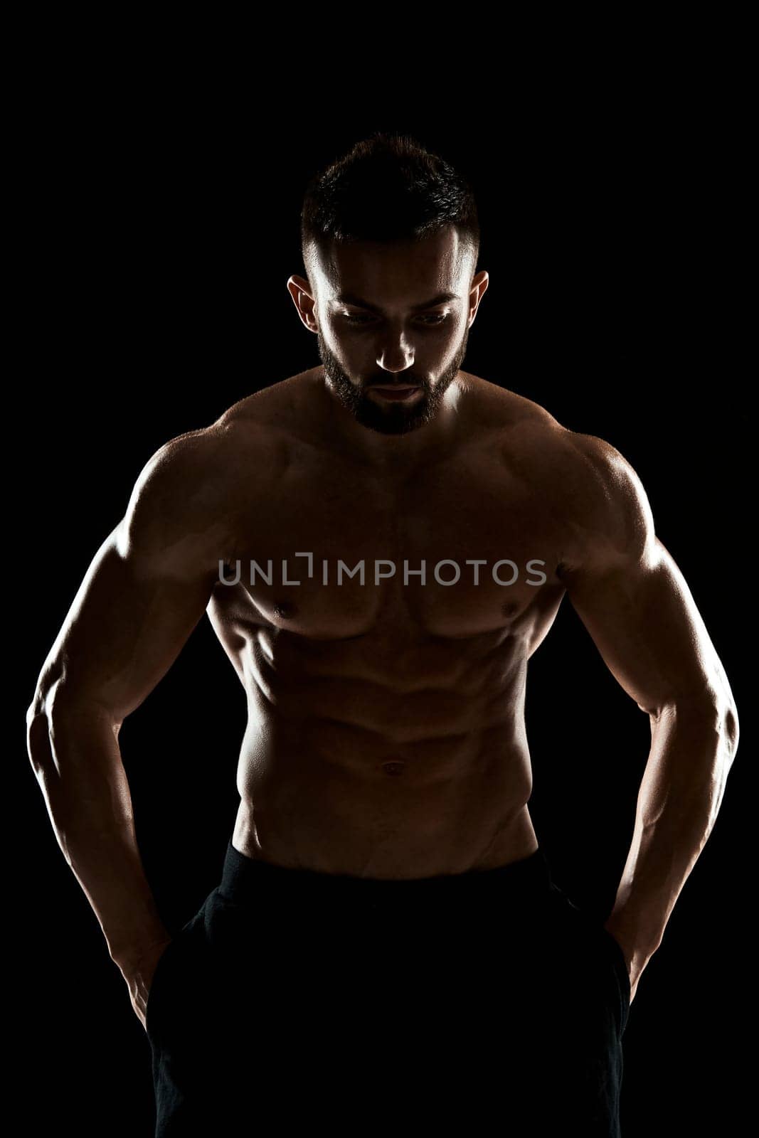 Image of very muscular man posing with naked torso in studio on black background.