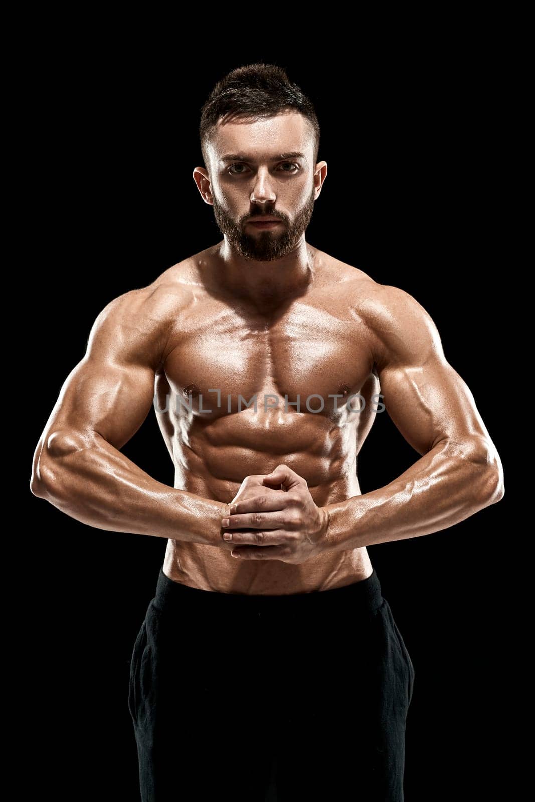 Image of very muscular man posing with naked torso in studio on black background.