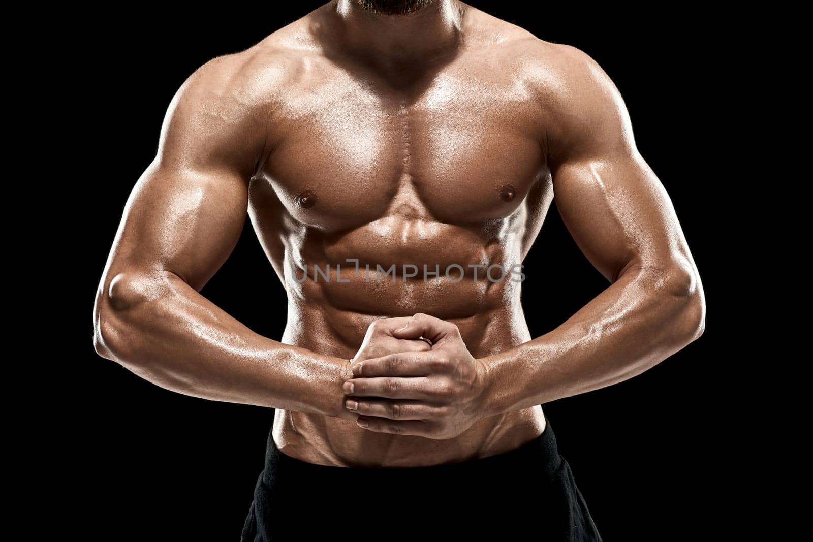 Image of very muscular man posing with naked torso in studio on black background.