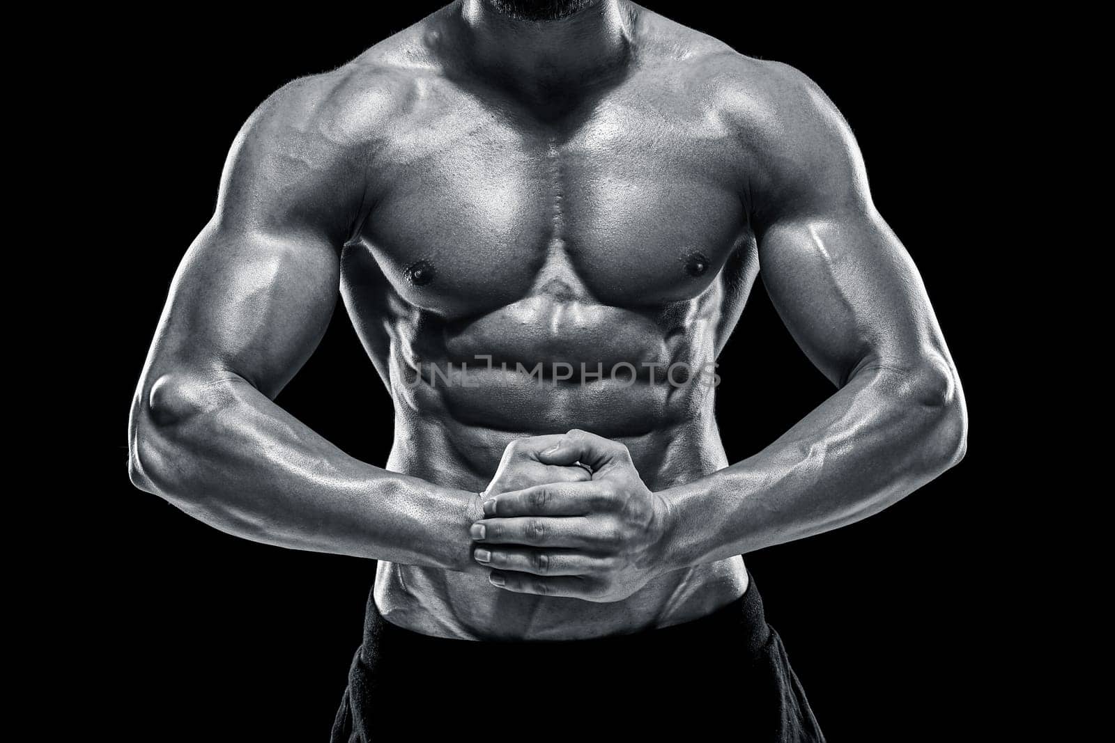 Image of very muscular man posing with naked torso in studio on black background. Black and white color