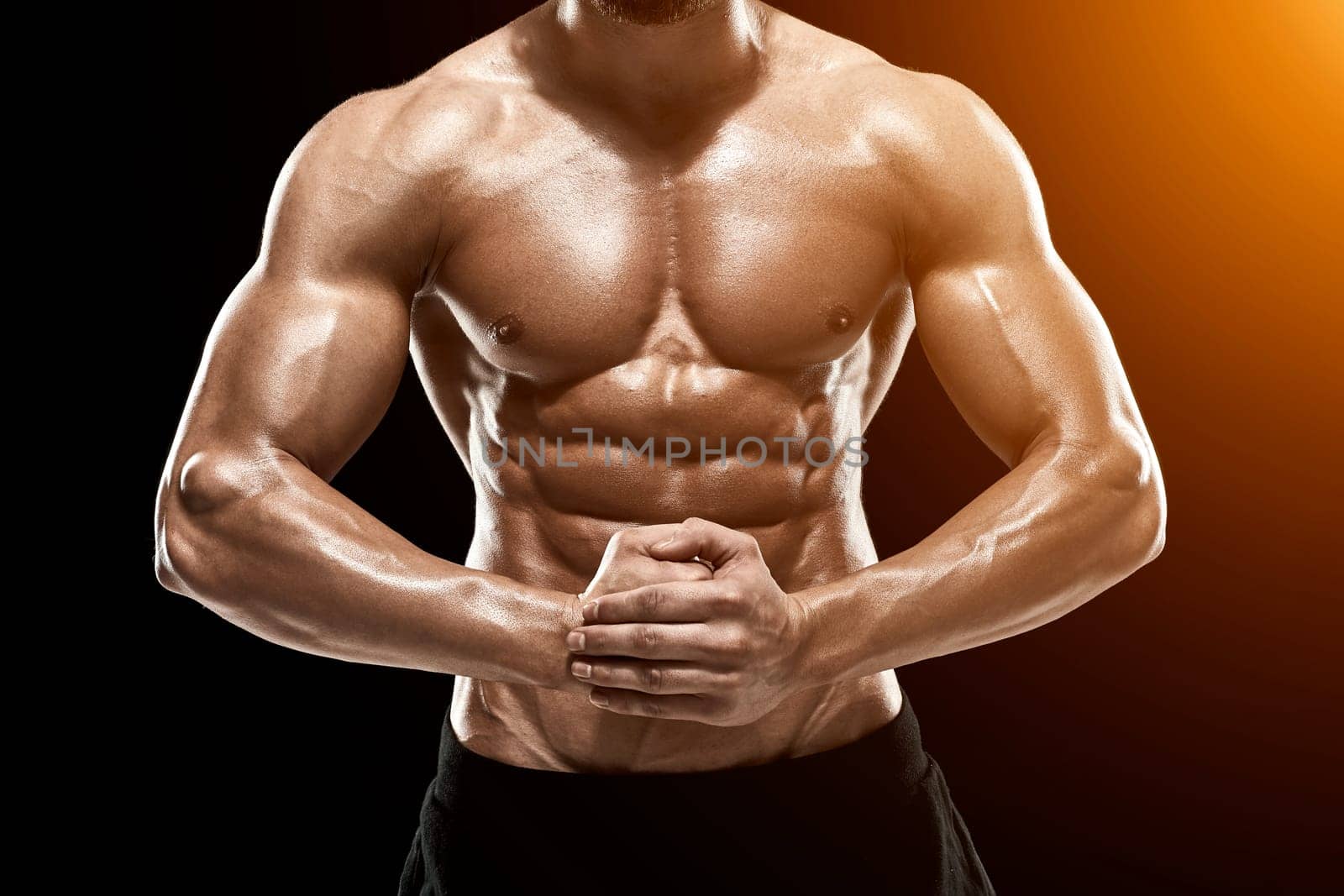 Image of very muscular man posing with naked torso in studio on black background.. with sun flare