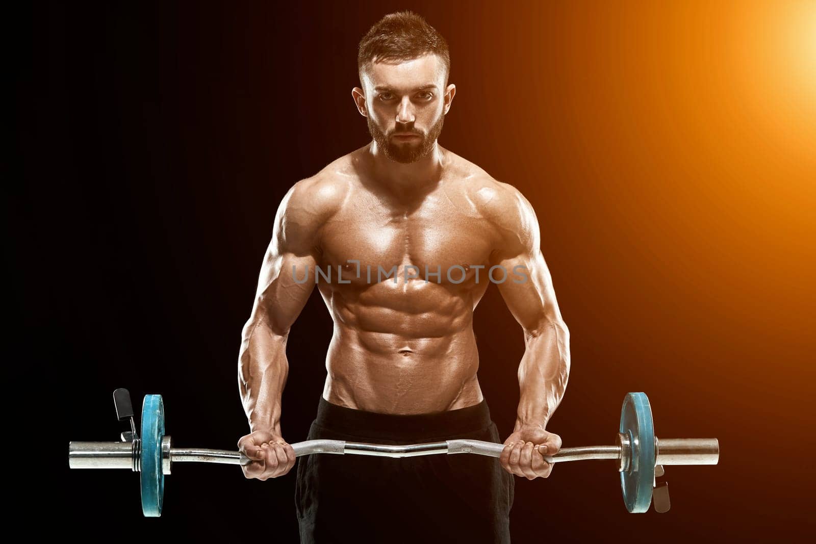 Close up of young muscular man lifting weights over dark background. with sun flare