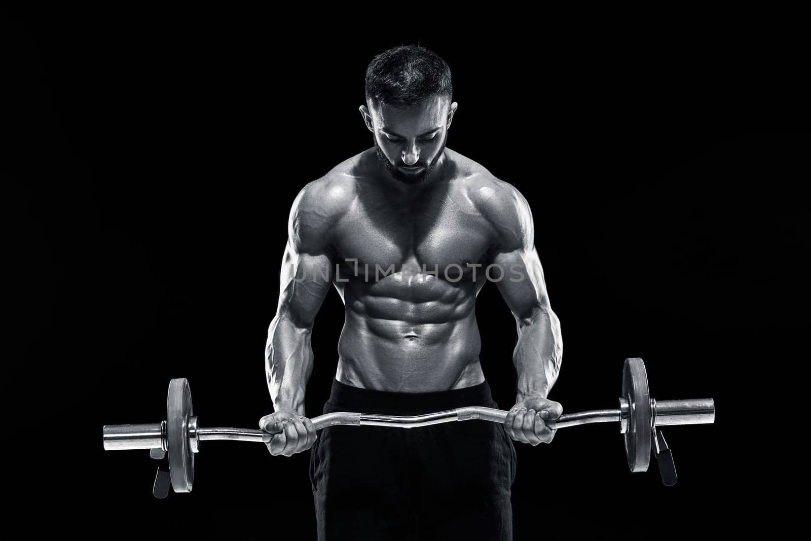Close up of young muscular man lifting weights over dark background. Black and white color