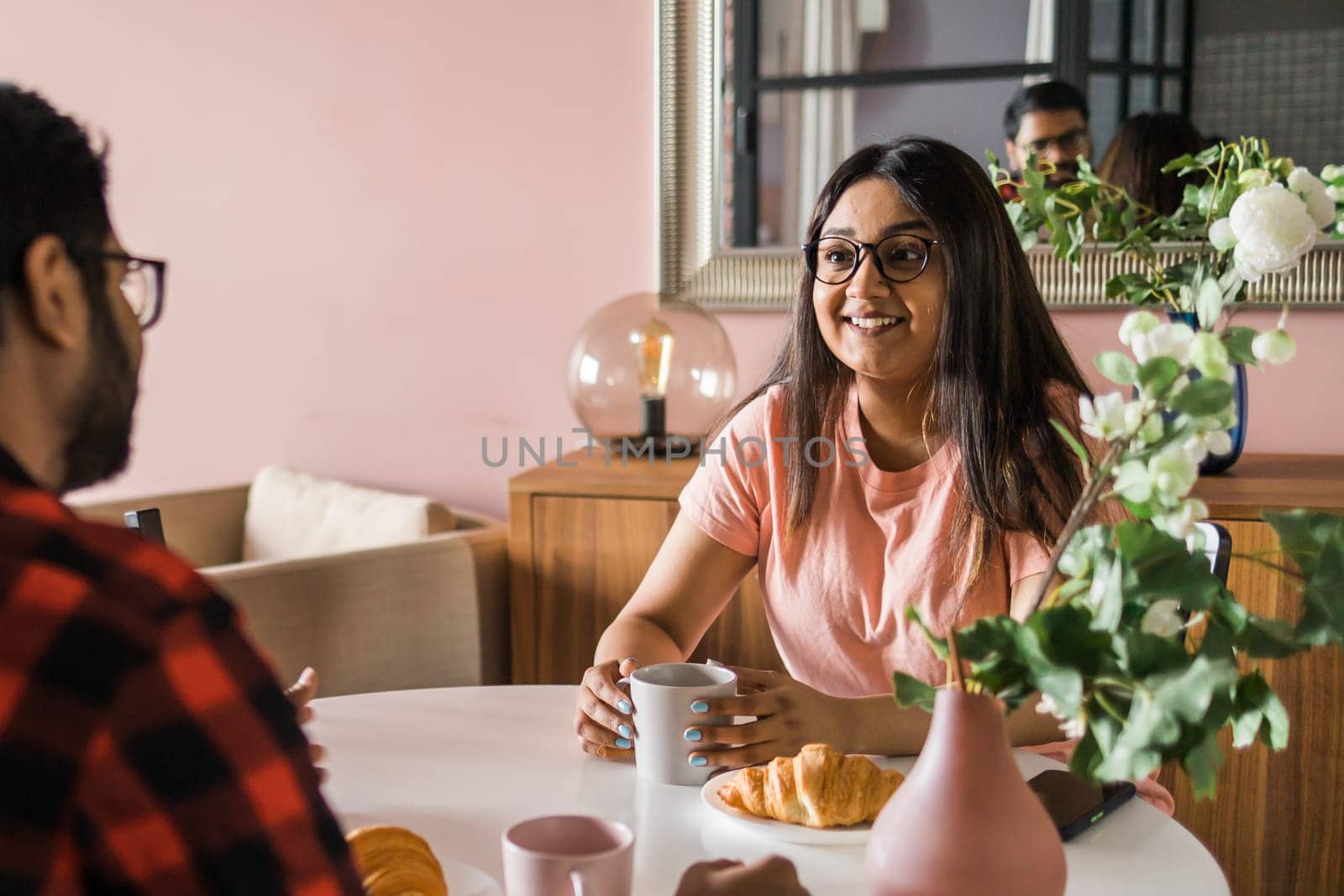 Young diverse loving couple eating croissant and talks together at home in breakfast time. Communication and relationship