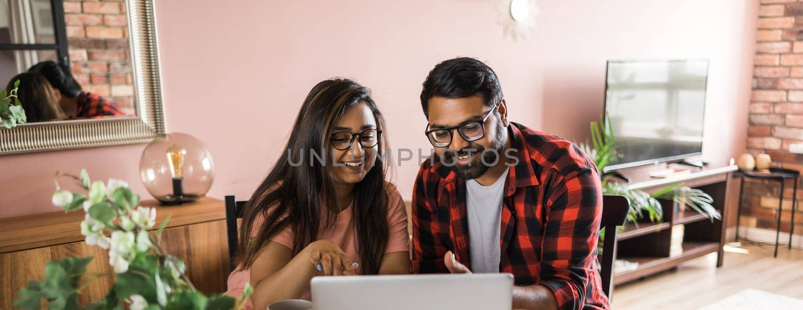 Banner Latino or indian man and woman couple use their laptop in the living room to make video calls copy space. Video call and online chat with family by Satura86