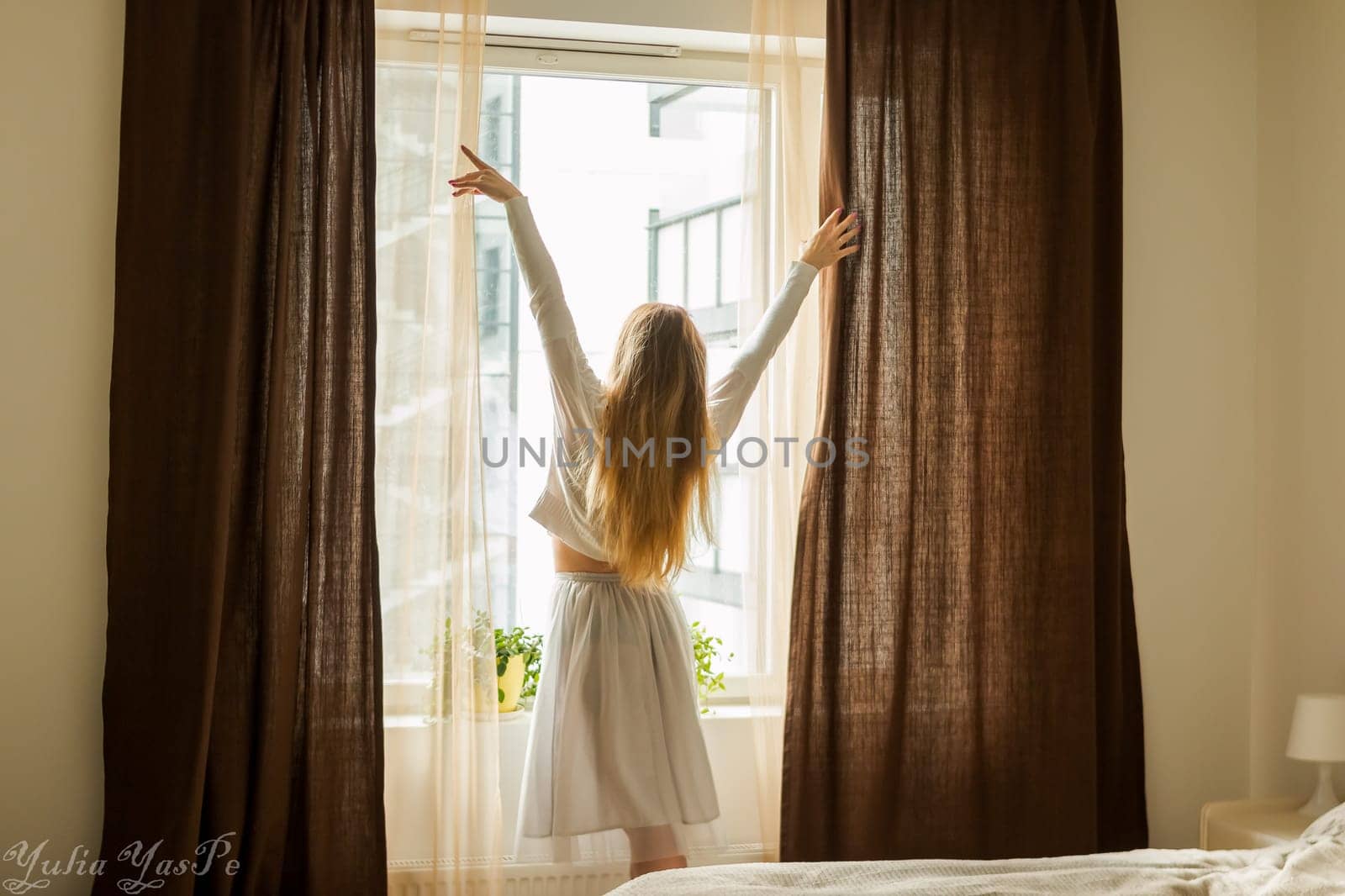 Hand Opens Curtain on the Wooden Cottage House Window. Bright Sunlight Shines Through. Beautiful snowy Winter morning light behind the Chalet Window.