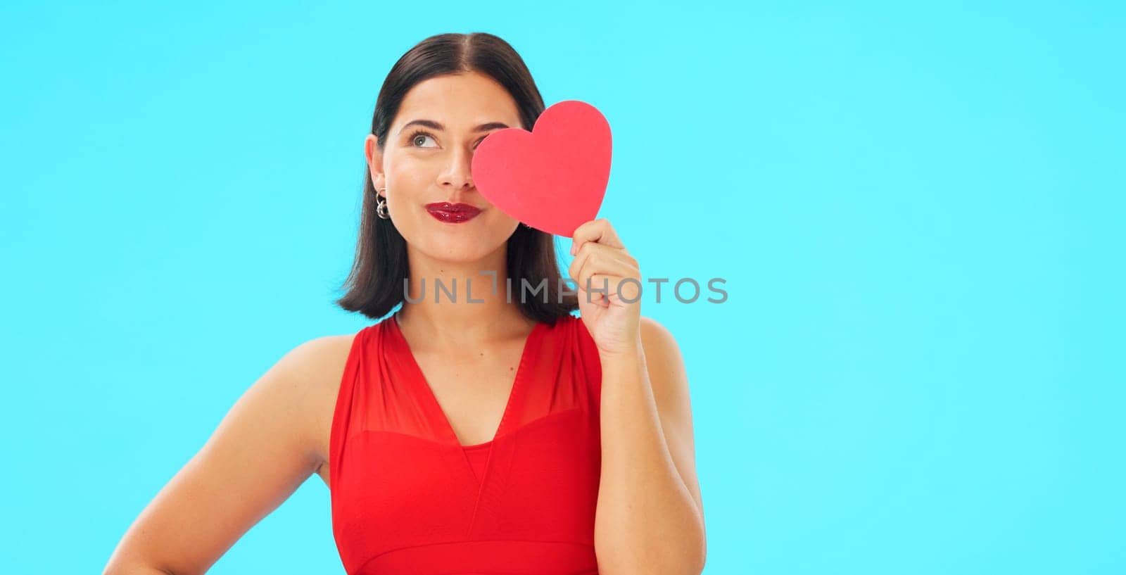 Paper heart, happy woman and face on blue background, studio and backdrop. Portrait of female model in red dress with shape of love, trust and romance for valentines day, flirting and elegant smile.