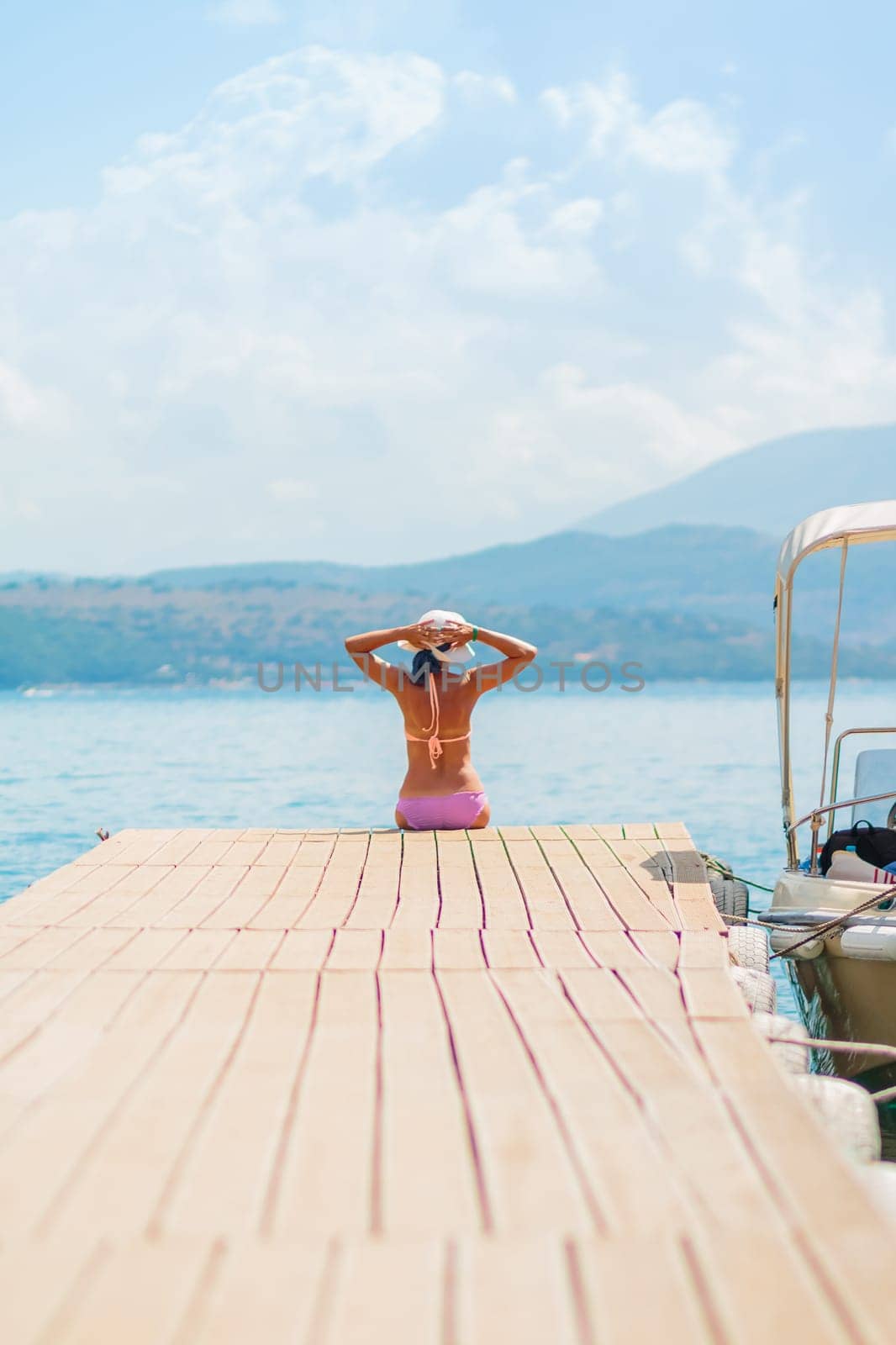 Woman with sunburned back sit on wooden jetty while looking at the sea