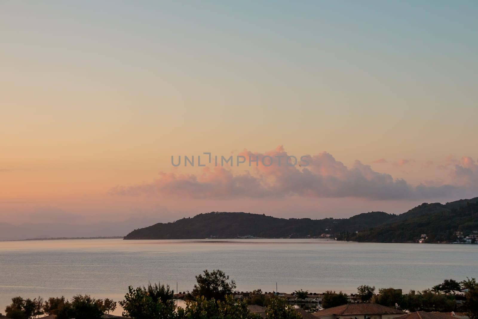 Colorful vanilla sky under calm silver sea and rocky mountains at dawn