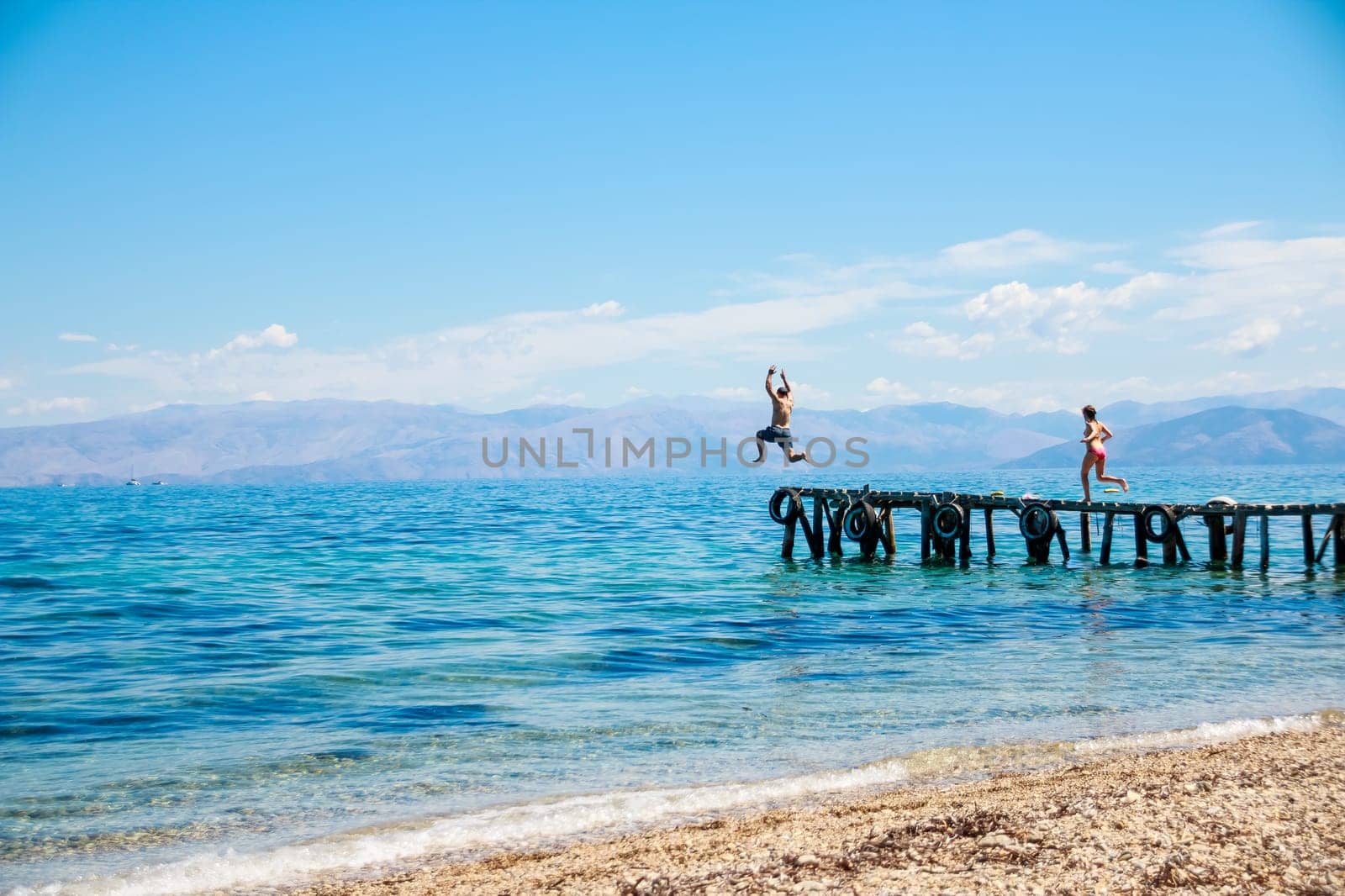 Group of teenagers jumping off the pier into the sea. fun summer vacation