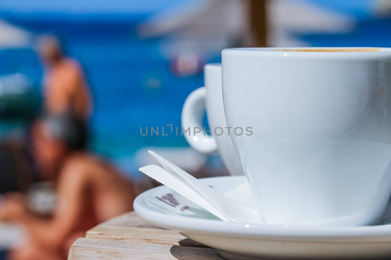 Coffee cup on round table in cafe terrace on the old pier with rusty railing and the view on the sea with waves in sunny day.