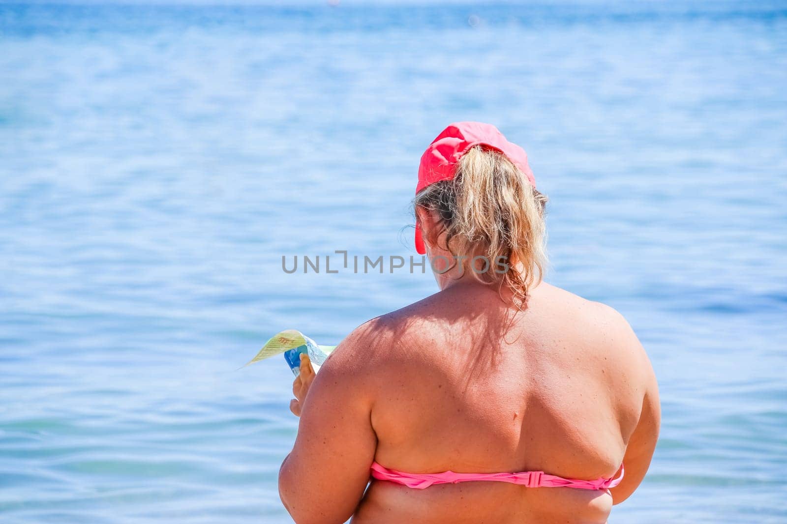 mature woman in swimwear at the sea. Overweight woman in swimsuit comes in water in time of surf, rear view